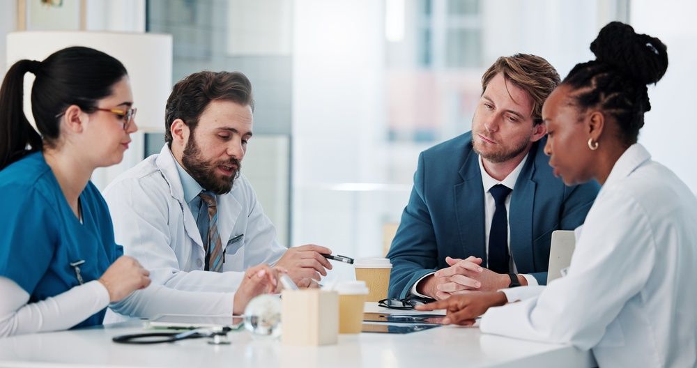 Four coworkers in a meeting, leaning over papers at a conference table in a bright office.