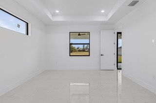 Empty, white-walled room with a rectangular window, a door, and a tiled floor. Bright natural light floods the space.