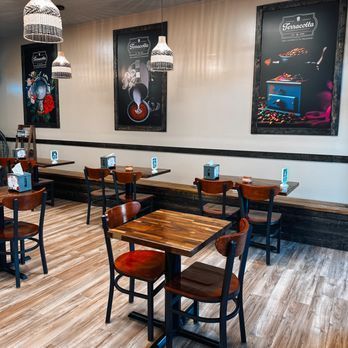 Interior of a coffee shop: tables, chairs, two large posters, pendant lights, wood floors.