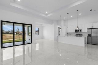 Modern, bright open-concept living space with white kitchen, large glass doors, and stainless steel appliances.