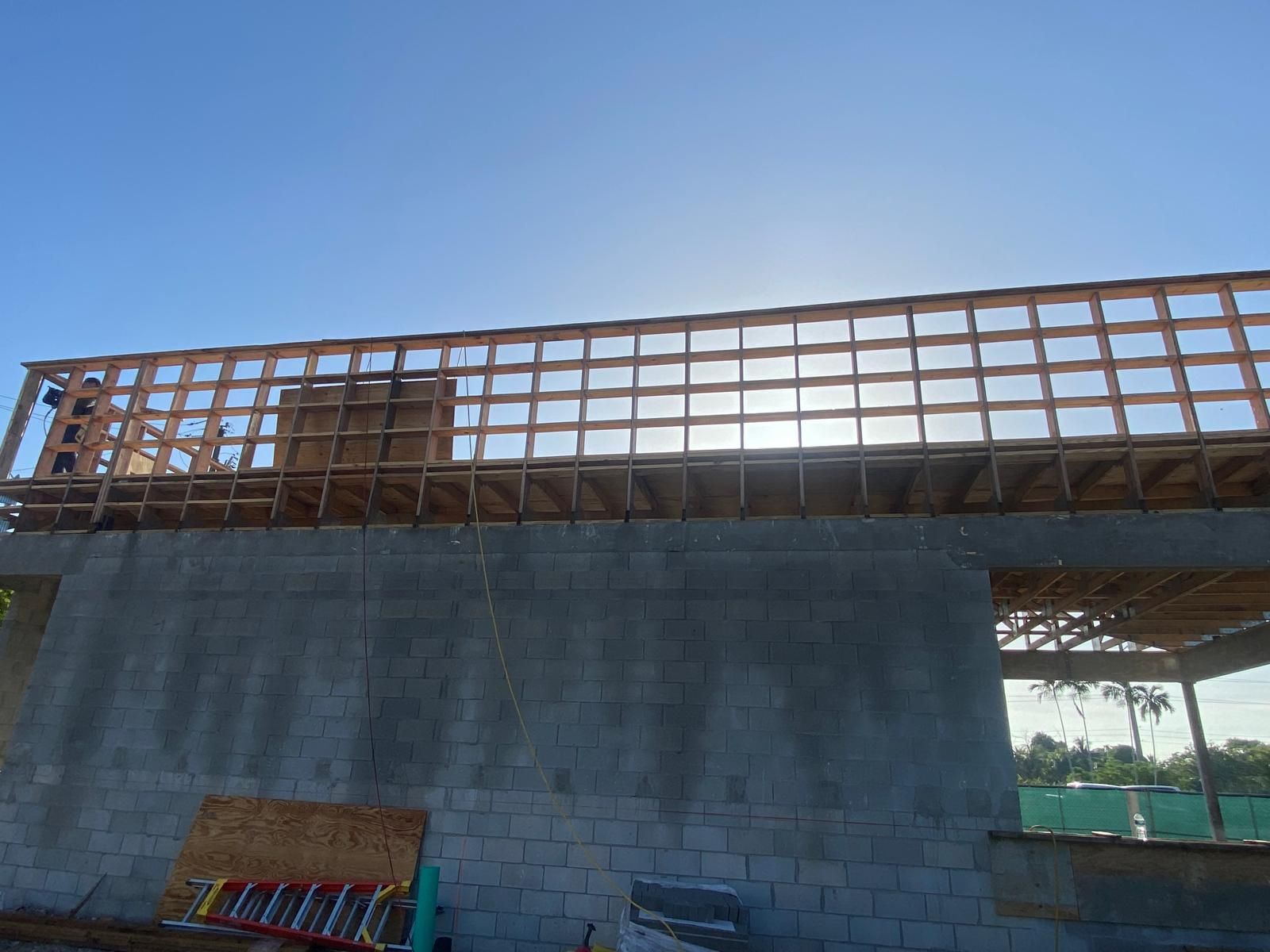 Construction of a building frame with a partially built roof, set against a bright, sunny sky.
