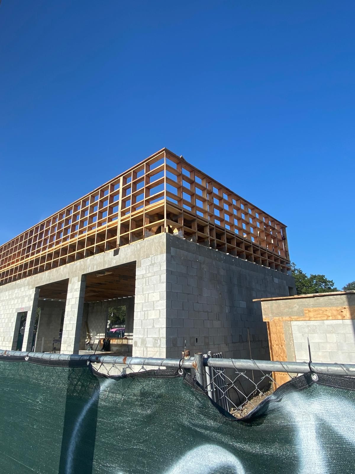 Construction site: concrete block building with wood framing for second level under clear blue sky.