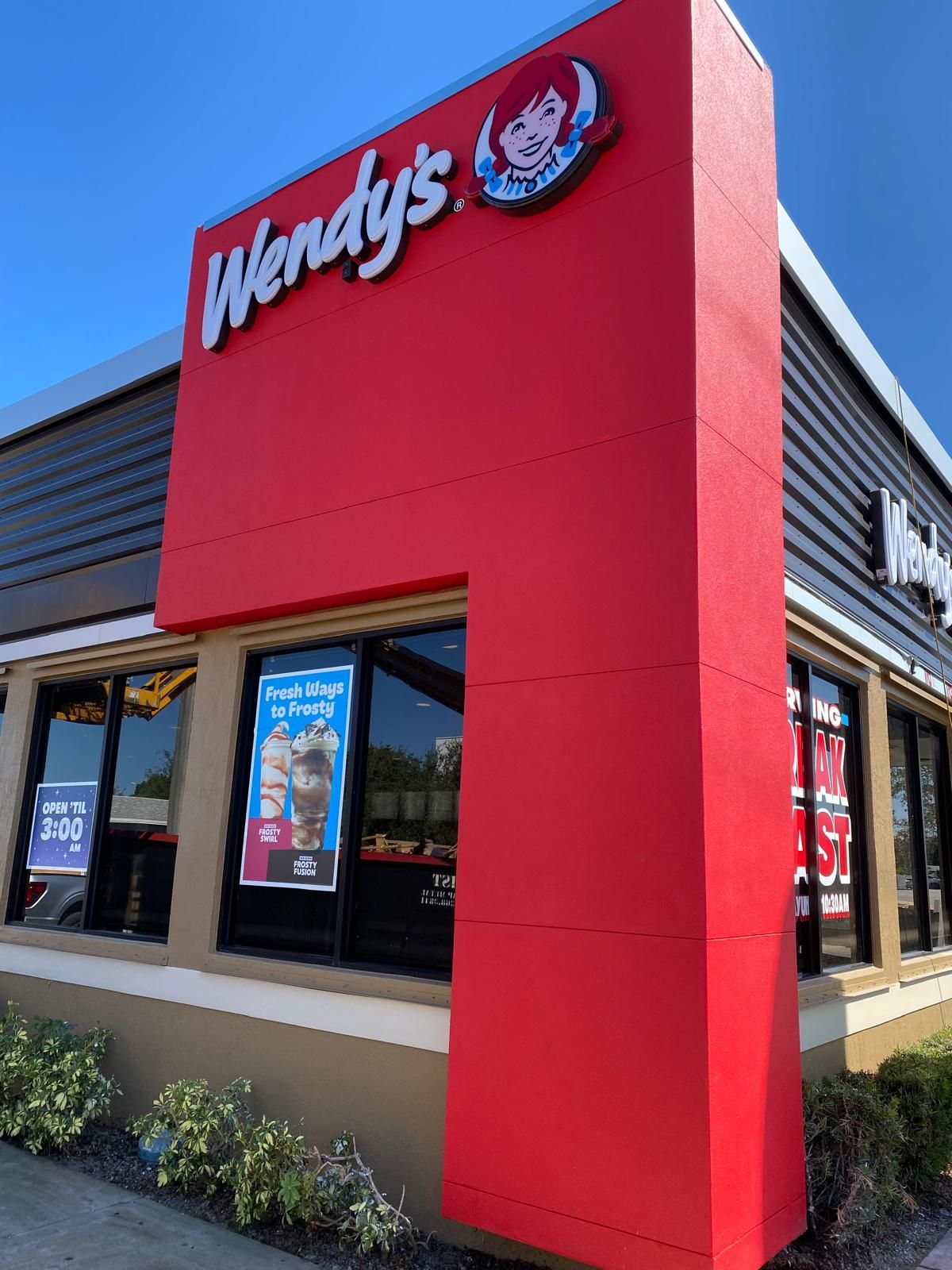 Wendy's fast-food restaurant exterior with red facade and logo, windows, and clear blue sky.