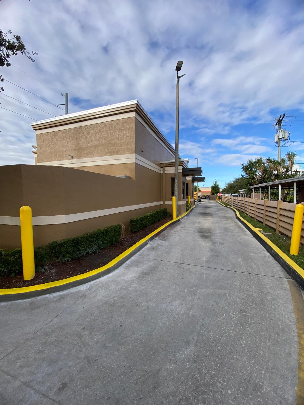 Drive-thru lane at a fast-food restaurant. Tan building with a drive-thru lane and yellow curb bumpers under a blue sky.