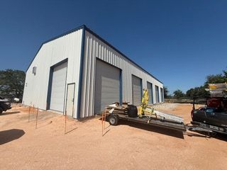White metal warehouse with blue trim and multiple garage doors on a red dirt lot.