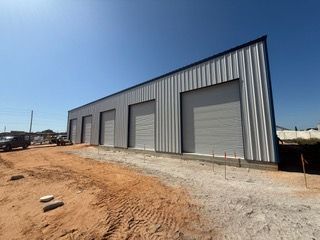 Metal warehouse under construction with four garage doors, against a clear blue sky.