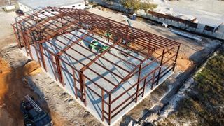Steel framework of a building under construction on a concrete foundation, outdoors.