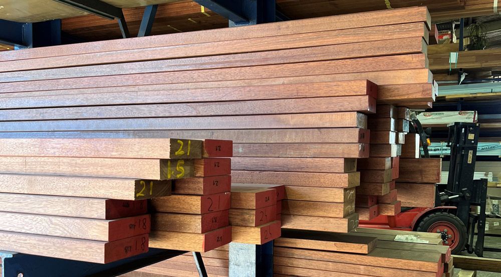 Stacks of long wooden beams piled in a workshop or lumber storage area. — B & B Timbers Ballina In West Ballina, NSW
