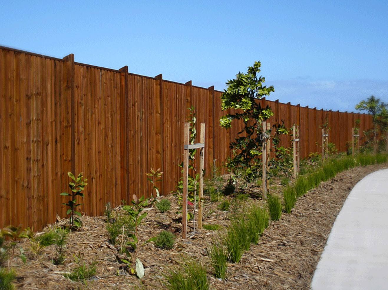 A Wooden Fence is Surrounded by Trees and Grass Along a Path — B & B Timbers Ballina In Murwillumbah, NSW