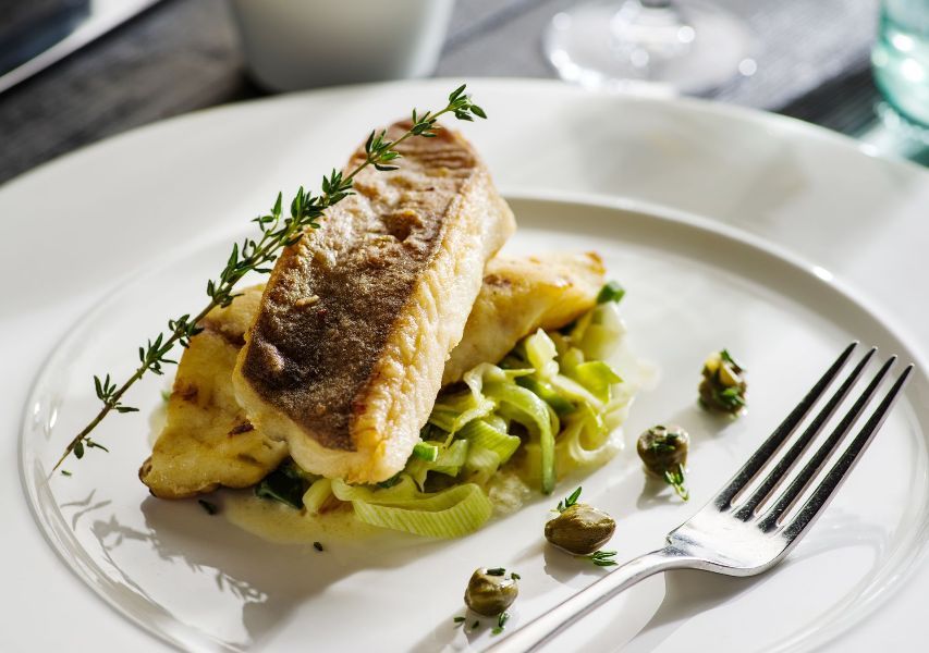 A white plate topped with a piece of fish and vegetables with a fork.