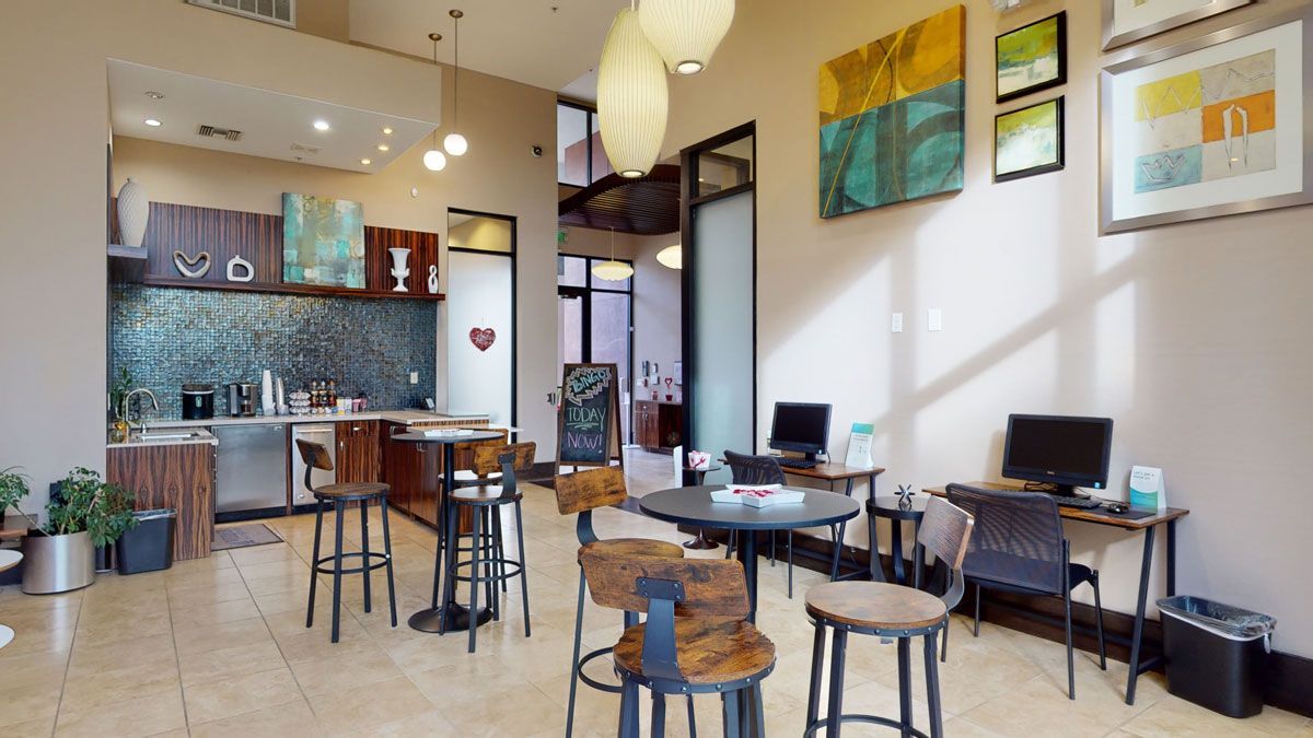A room with tables and chairs in it and a kitchen in the background.
