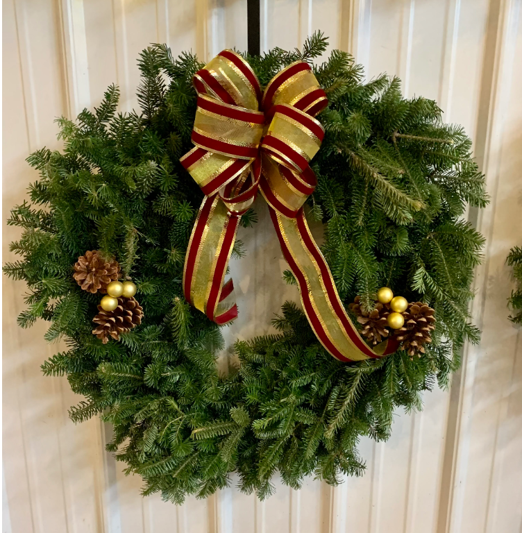 A round, lush green artificial Christmas wreath adorned with a red and gold ribbon bow, pinecones, and golden berries.