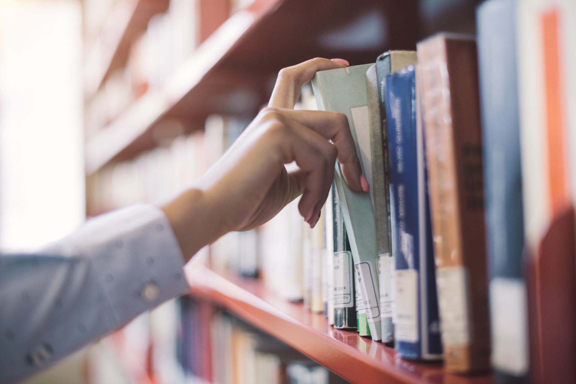 Hand reaching for a book on a library shelf.