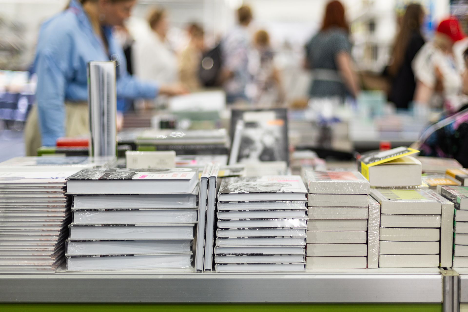 Books stacked on a table at a book fair, with blurred people in the background.