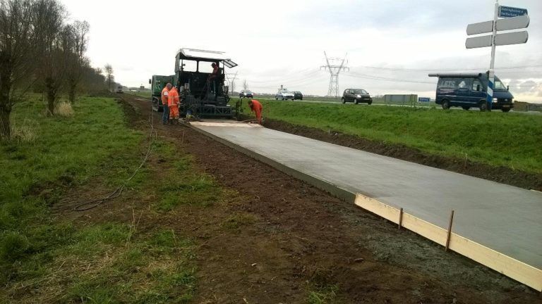 Een groep mensen legt beton aan de kant van een weg.