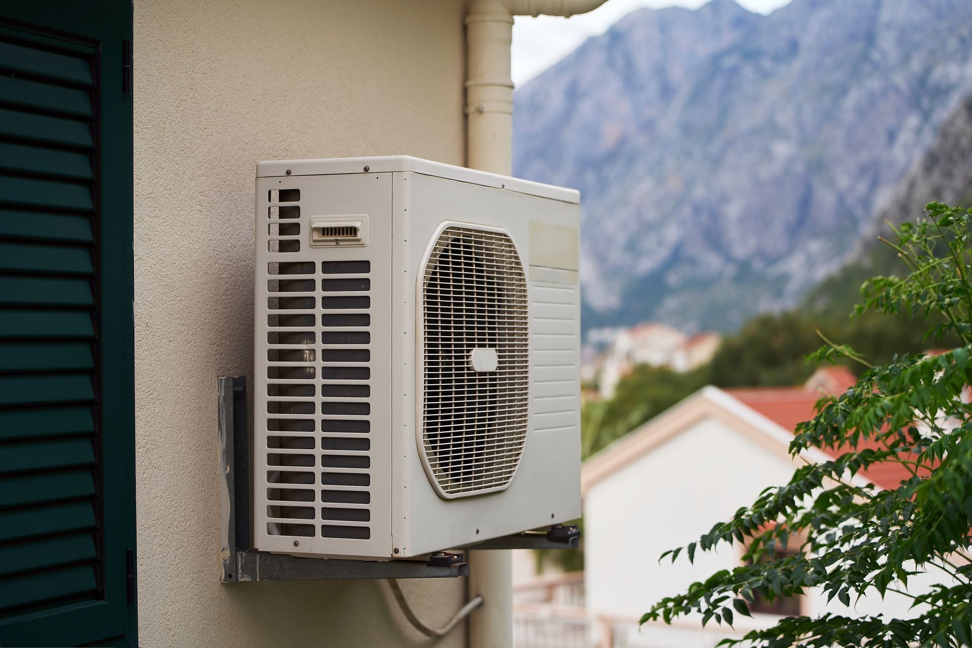 Outdoor air conditioner unit mounted on a building wall with mountains in the background