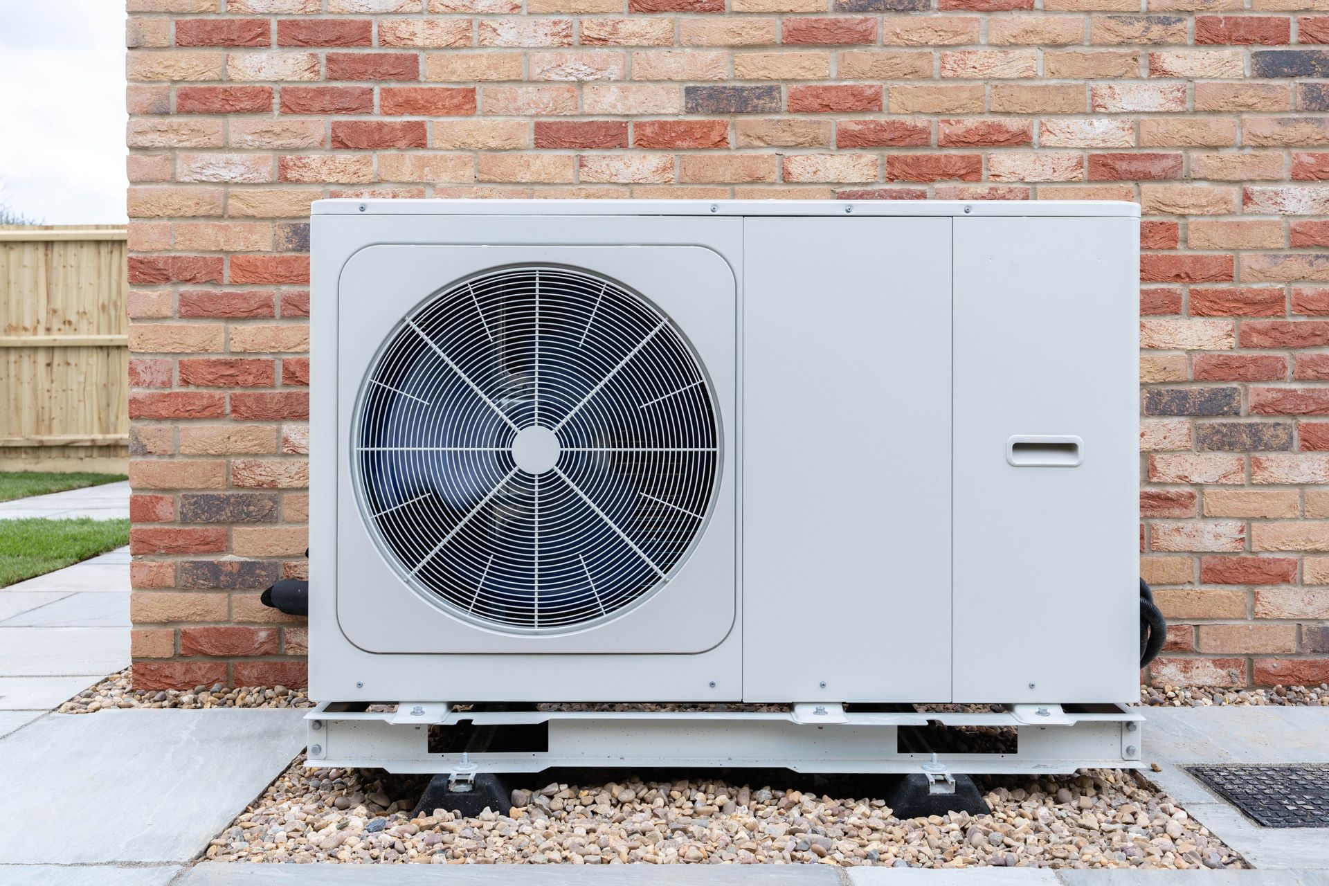 Outdoor heat pump unit beside a brick wall on a gravel pad