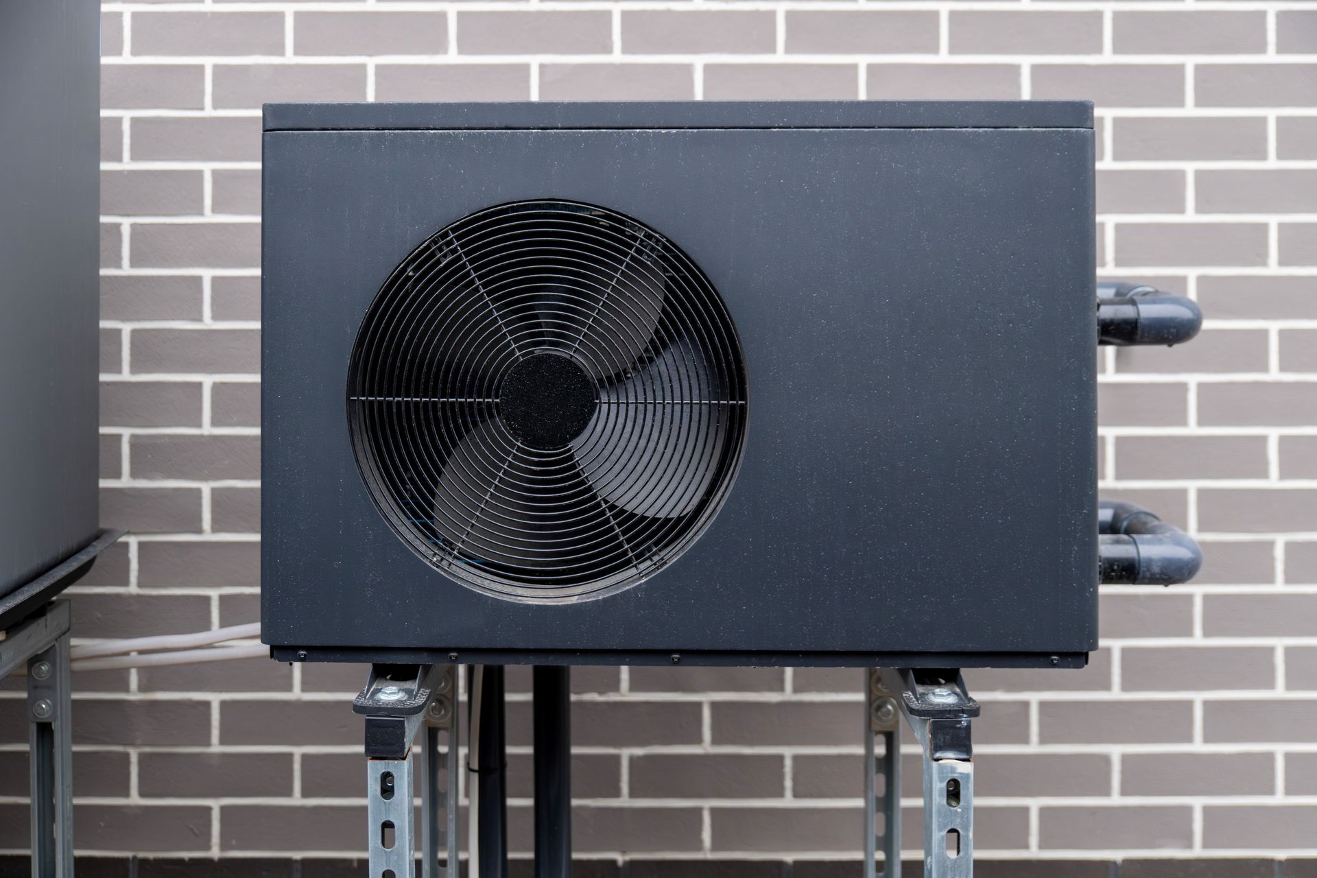 Black metal box with a large circular fan, mounted on a stand against a brick wall.