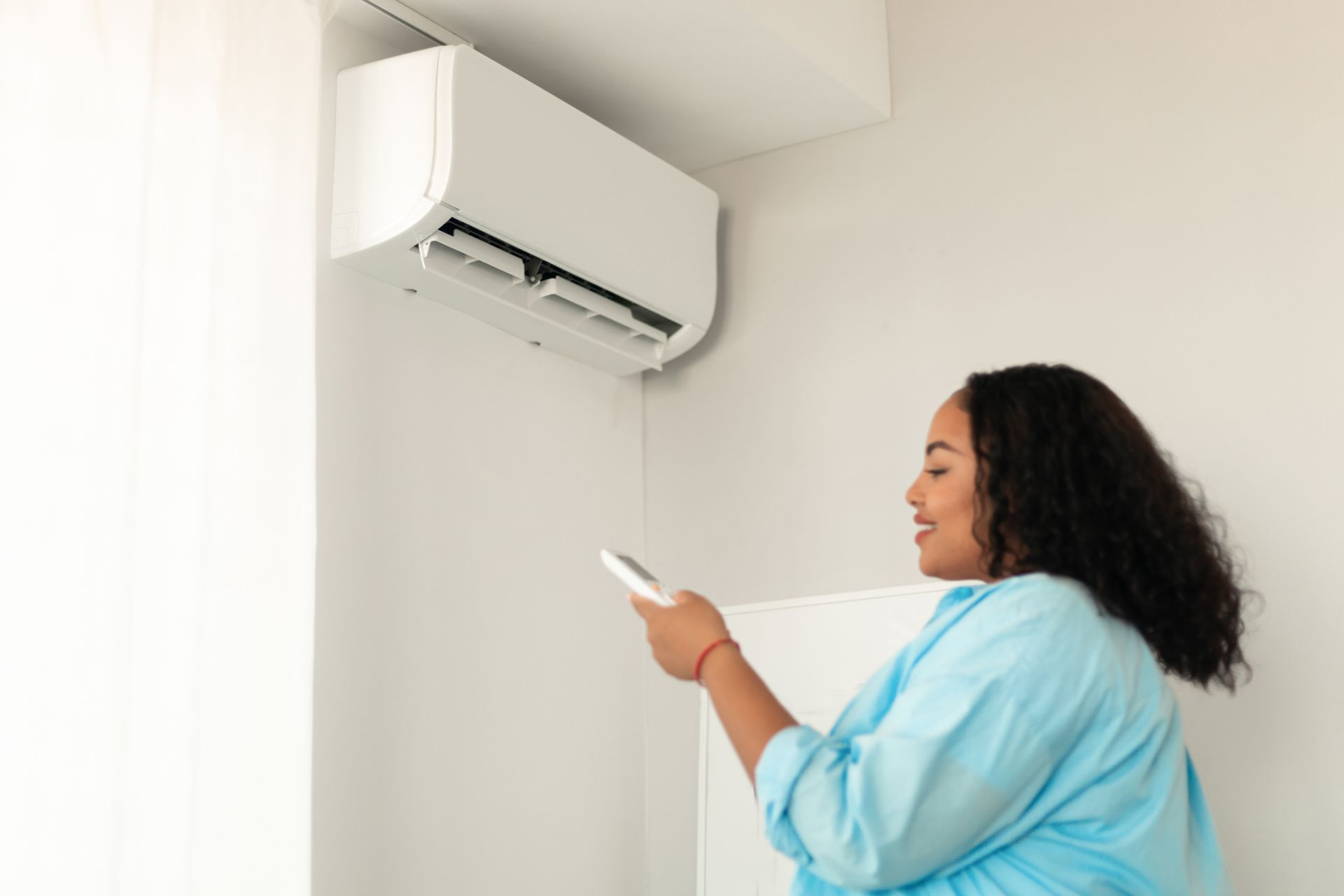 Woman using a remote to control a wall-mounted air conditioner in a bright room