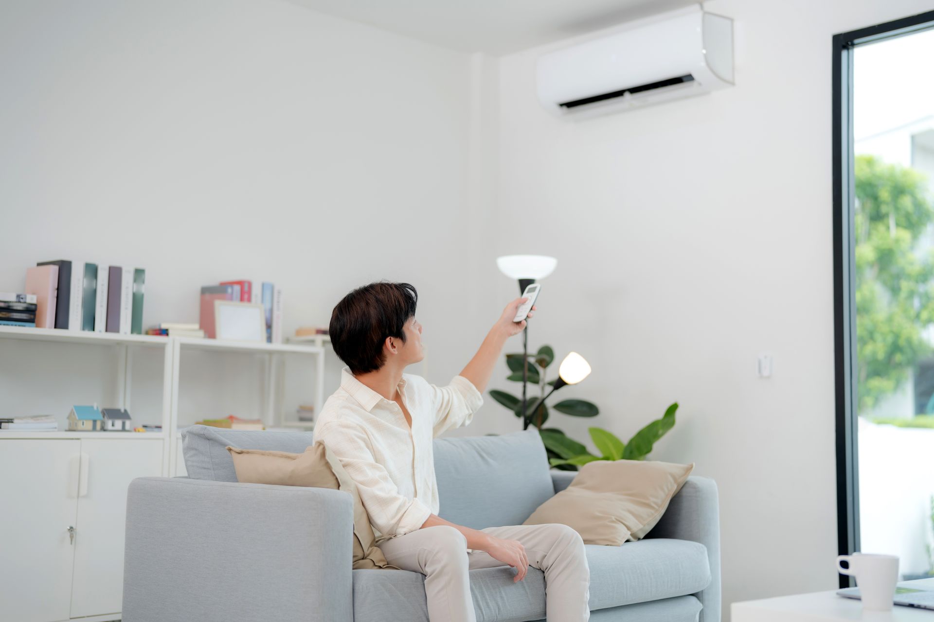 Person on sofa adjusting a lamp in a bright living room with white shelves and an air conditioner