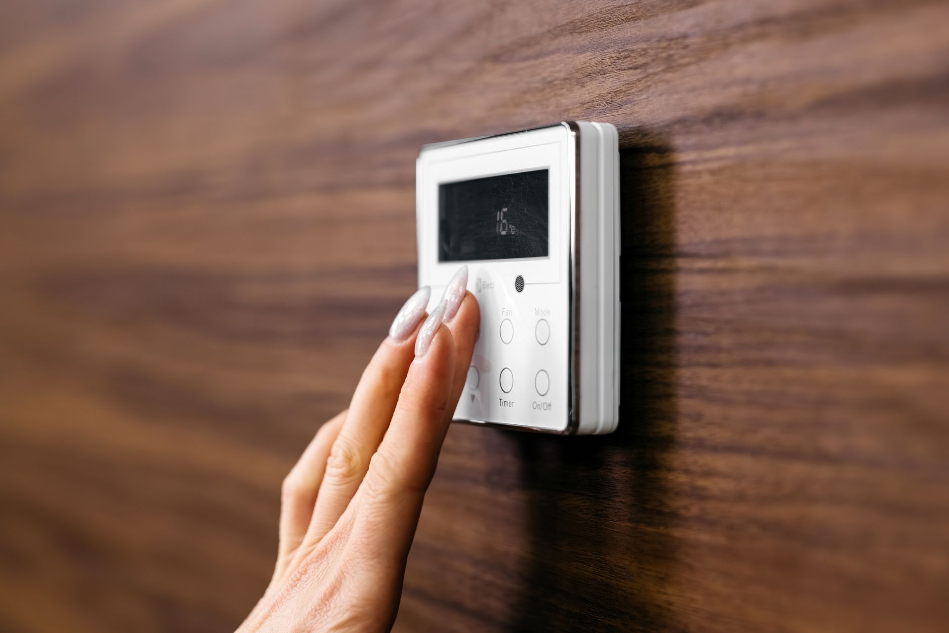 Hand turning a wall-mounted digital thermostat on a wooden wall
