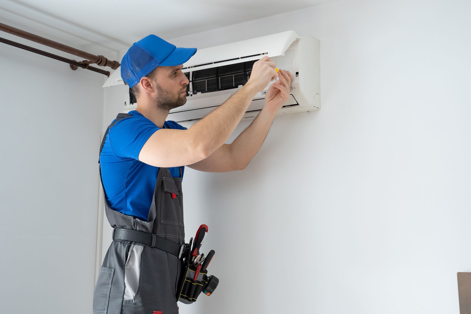 Technician cleaning a wall-mounted air conditioner in a white room.