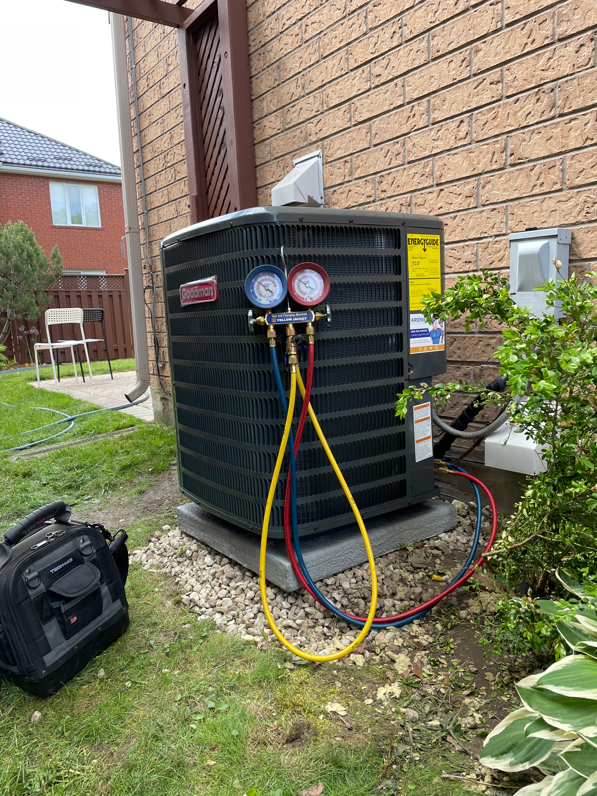 An air conditioner is being serviced in the backyard of a house.