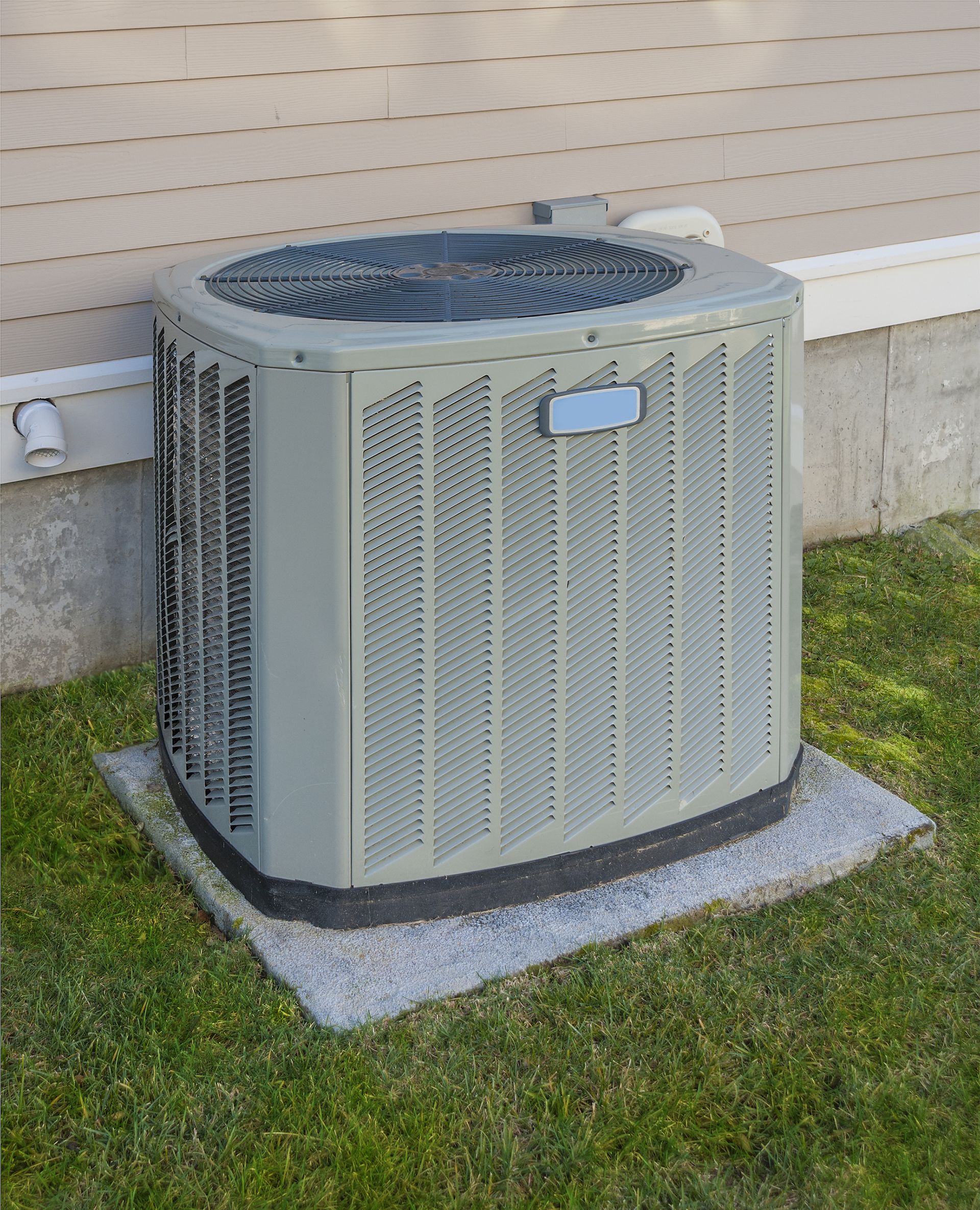 A gray air conditioner is sitting in the grass next to a house.