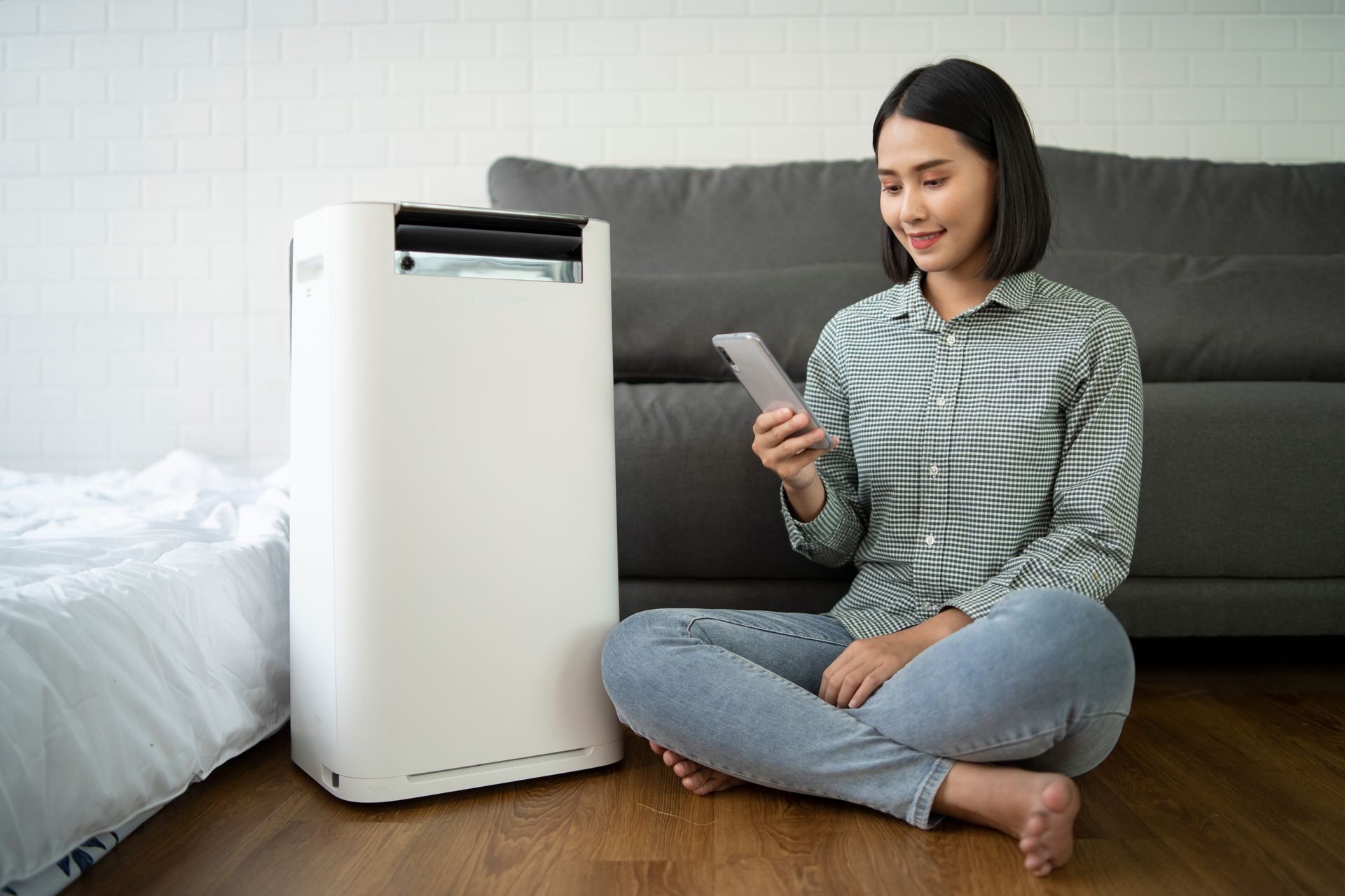 A woman is sitting on the floor next to a air purifier and using a tablet.
