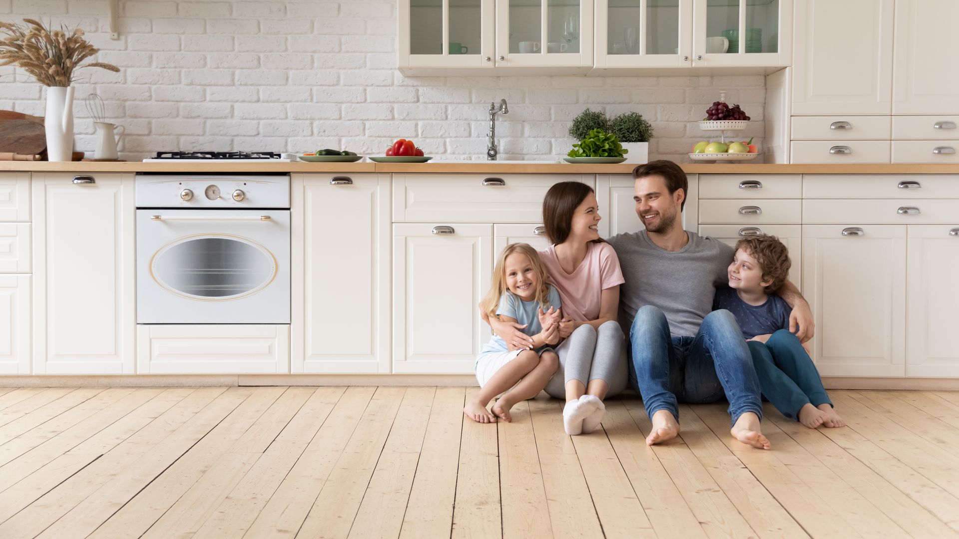 A family is sitting on the floor in a kitchen.