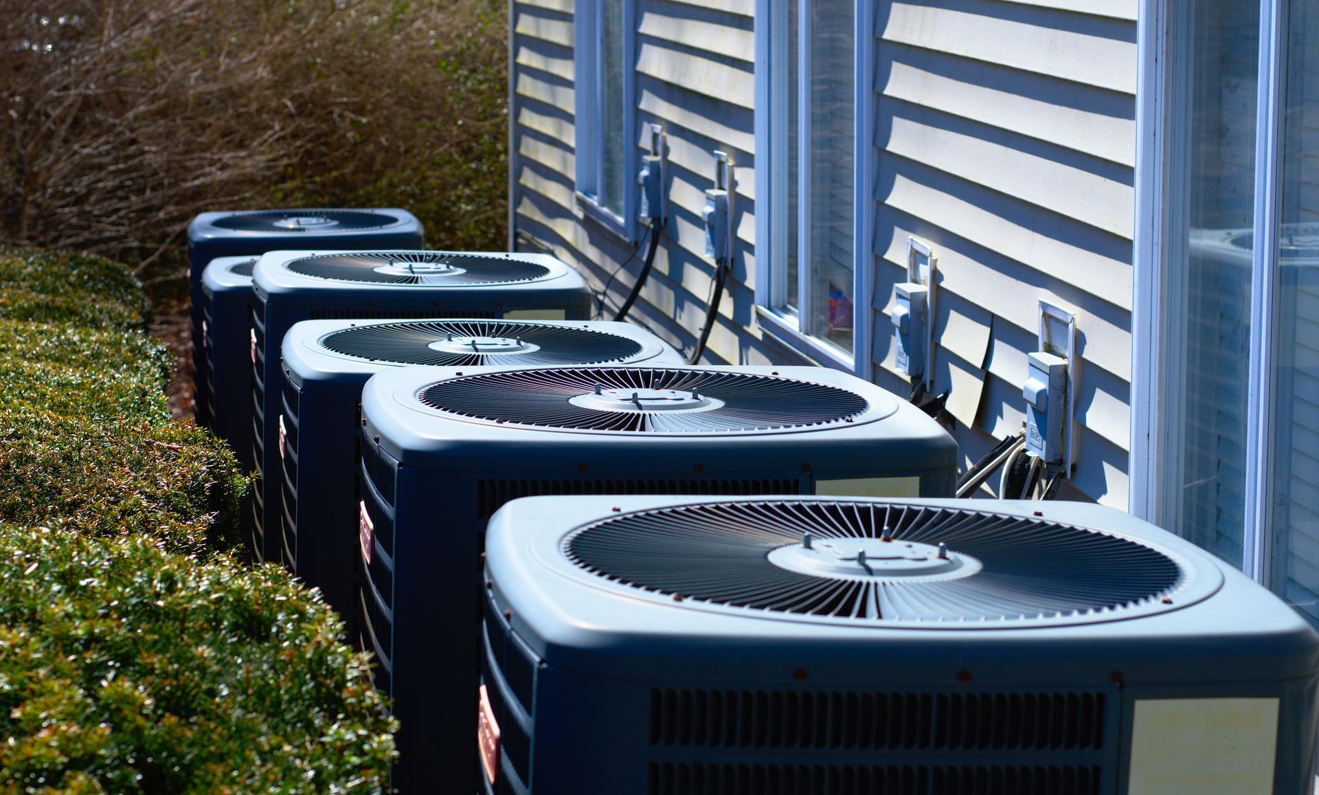 A row of air conditioners are lined up in front of a house.