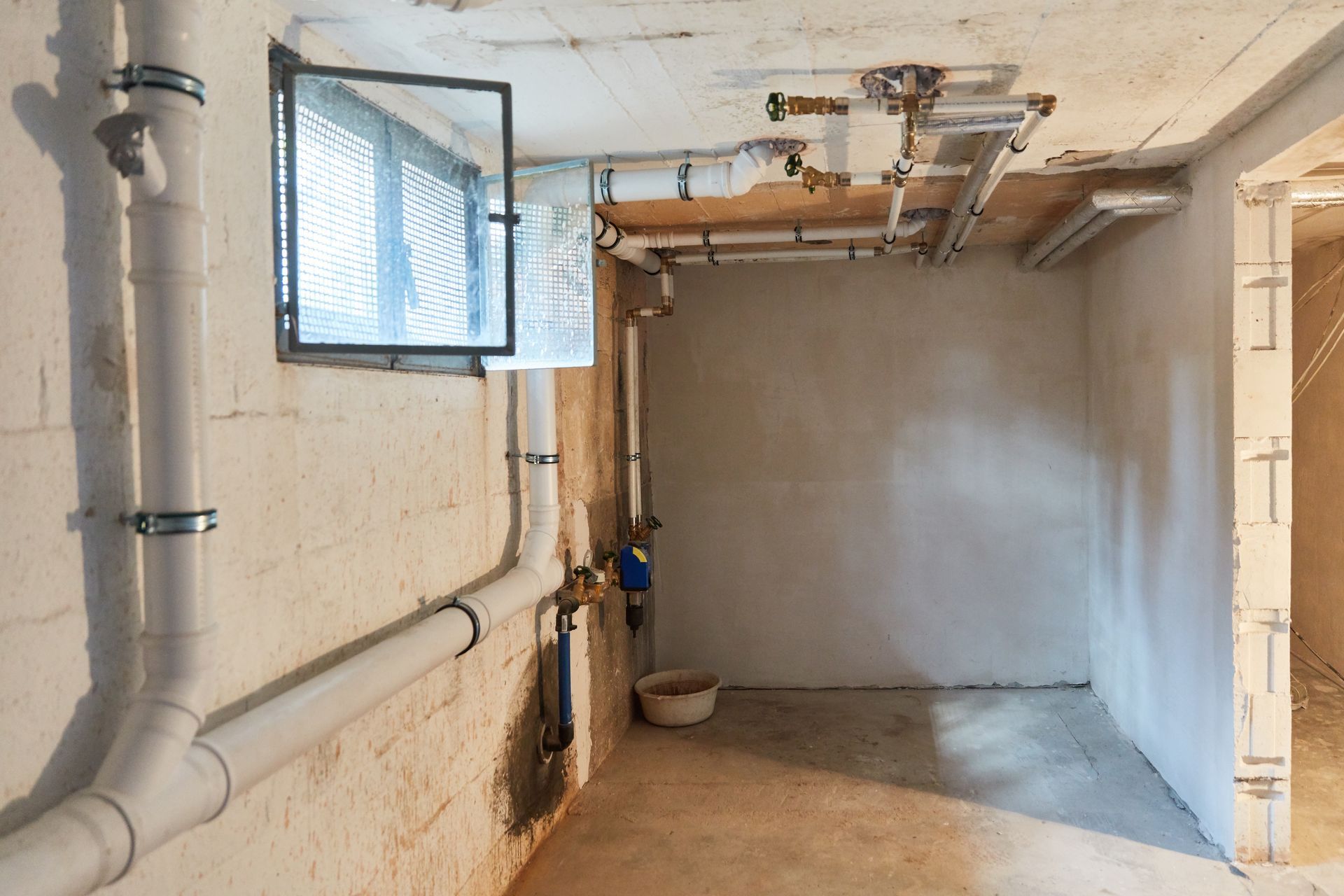 An empty basement with pipes and a window