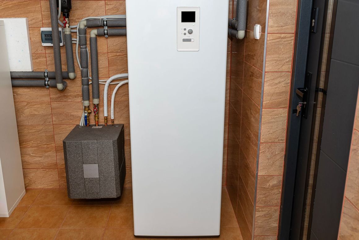 A white water heater is sitting in a room next to a brick wall.