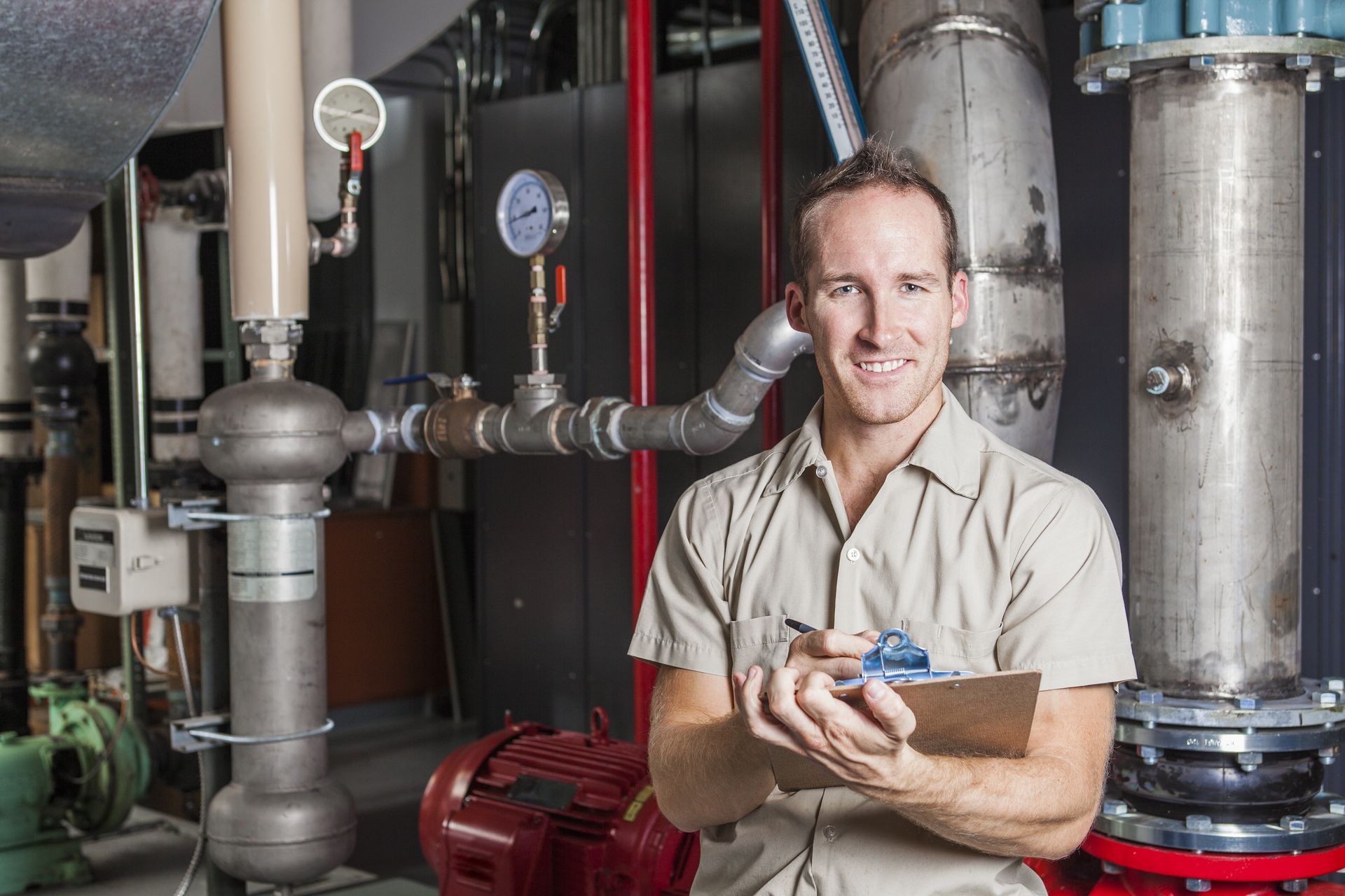 A man is standing in a room with pipes and holding a clipboard.
