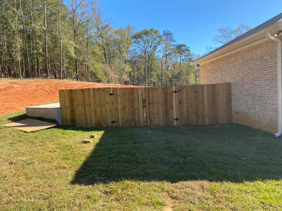 Wooden fence in backyard next to a brick building and grassy yard.
