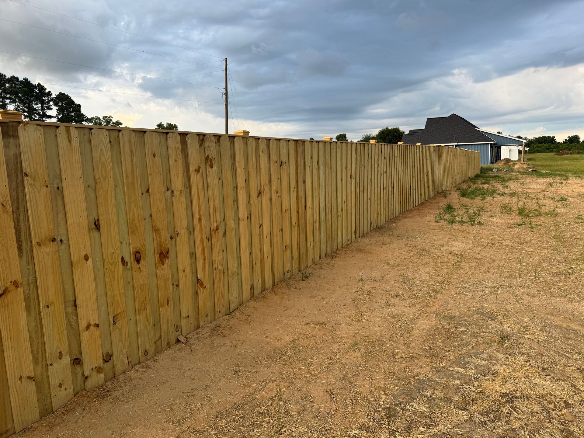 Wooden fence in an open field under a cloudy sky.