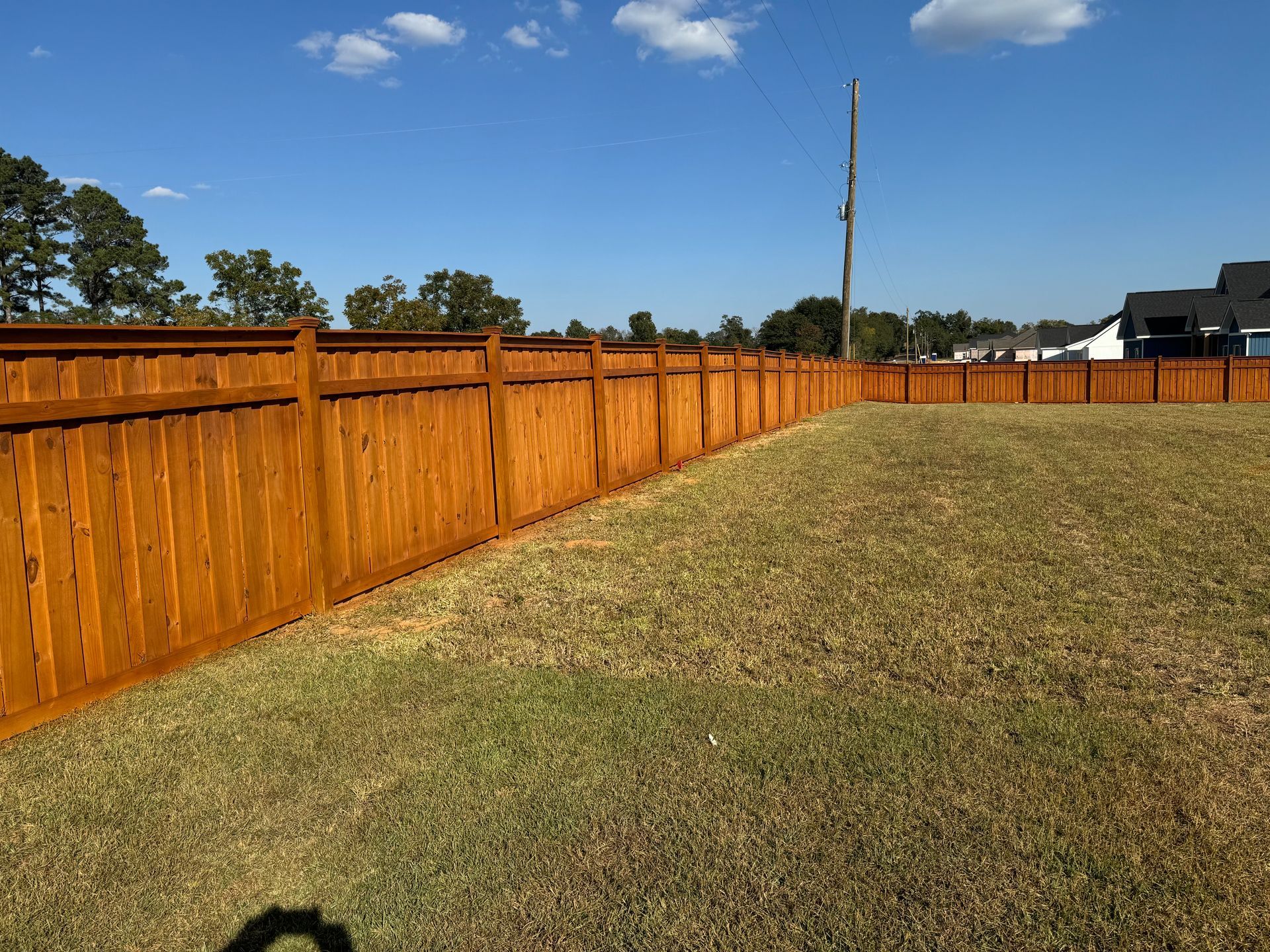 Wooden fence stained orange-brown surrounds a grassy yard on a sunny day.