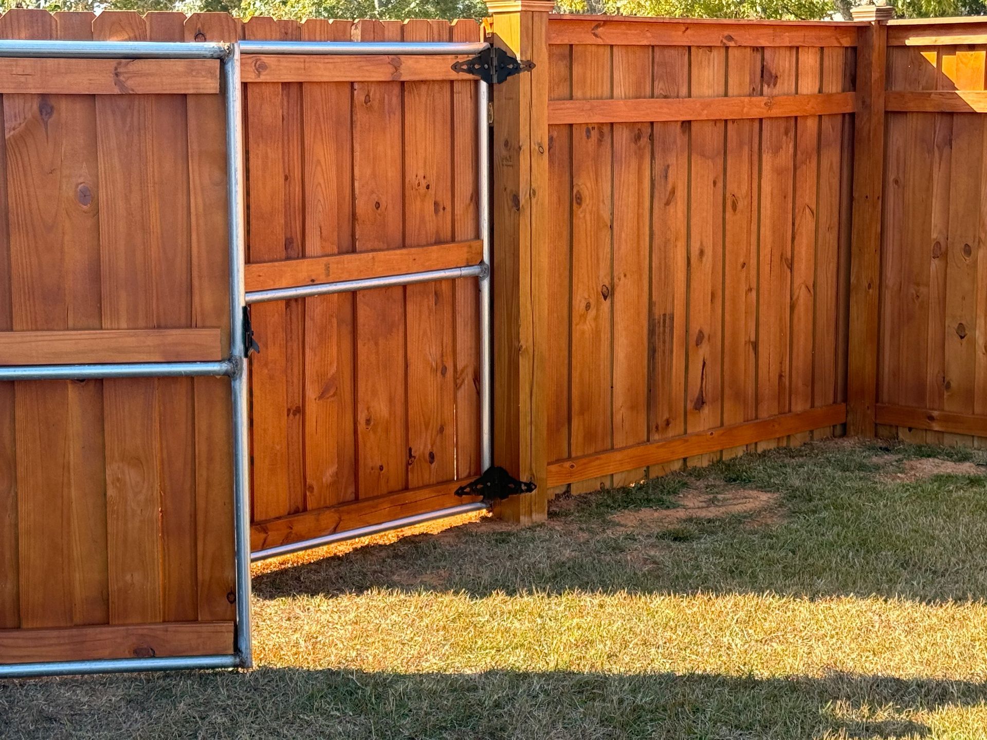 Wooden fence with gate, stained brown, on green grass.