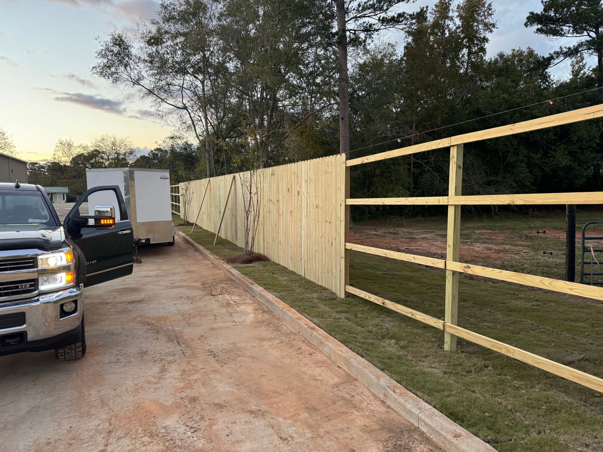 A new wooden fence alongside a road, with a truck and trailer parked nearby.