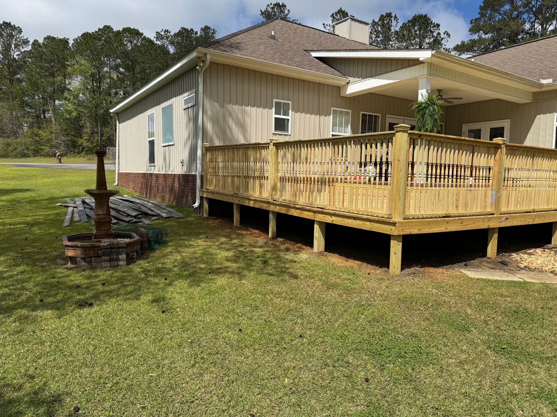 Wooden deck attached to a light-colored house; a fountain sits on the lawn.