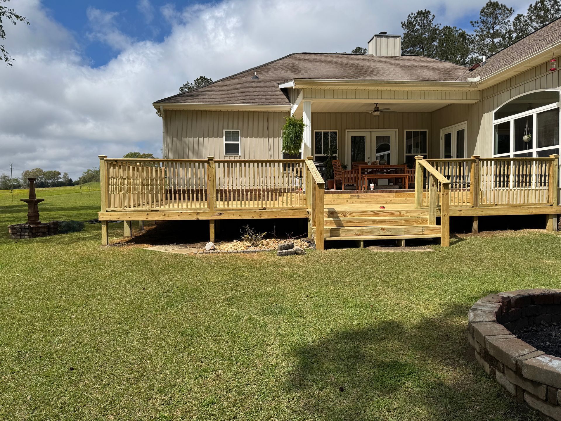 Wooden deck attached to a light-colored house with a grassy lawn in the foreground and a fire pit on the right.