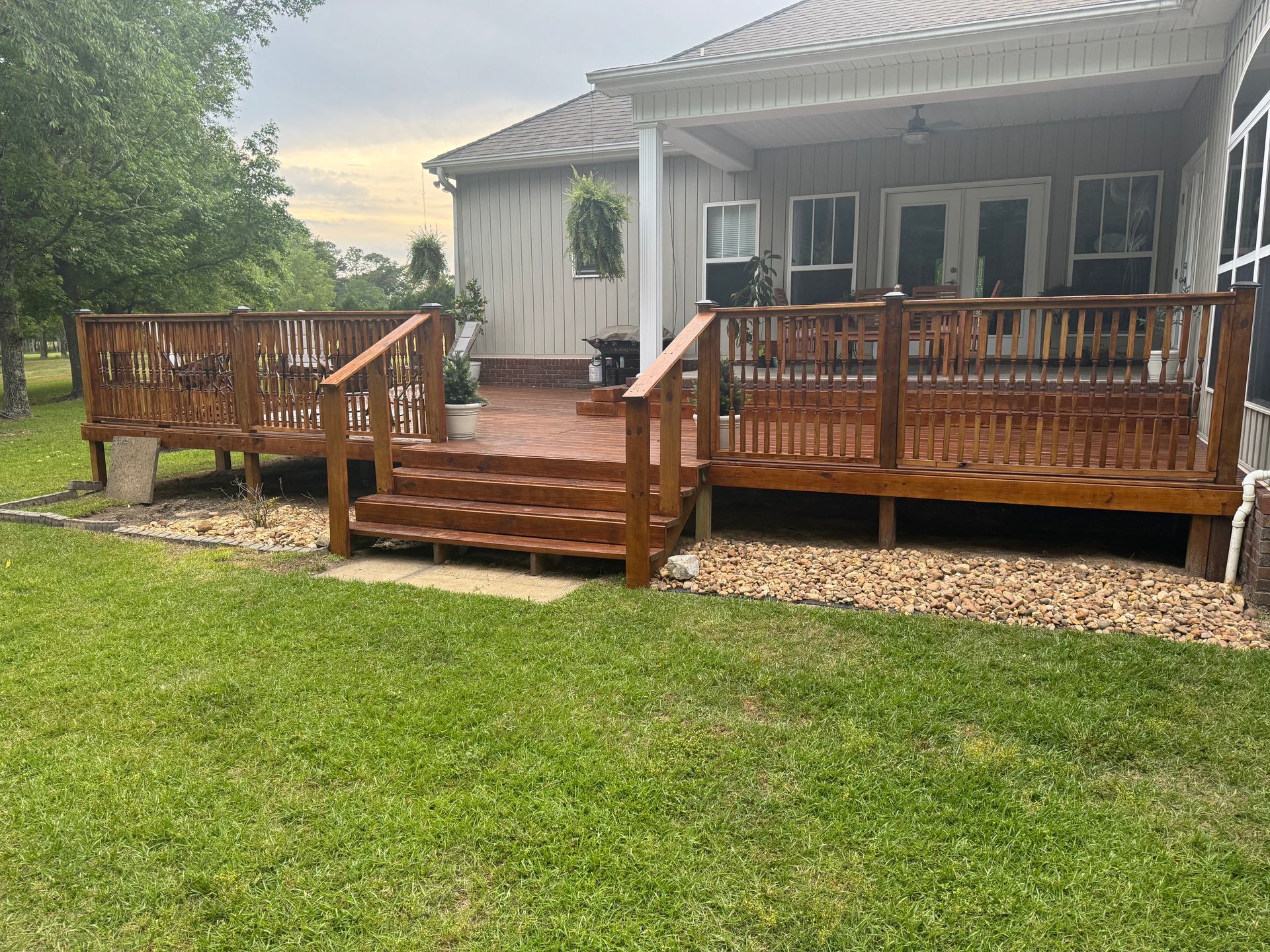Wooden deck extending from a house with stairs and railings. Stained brown with decorative gravel border.