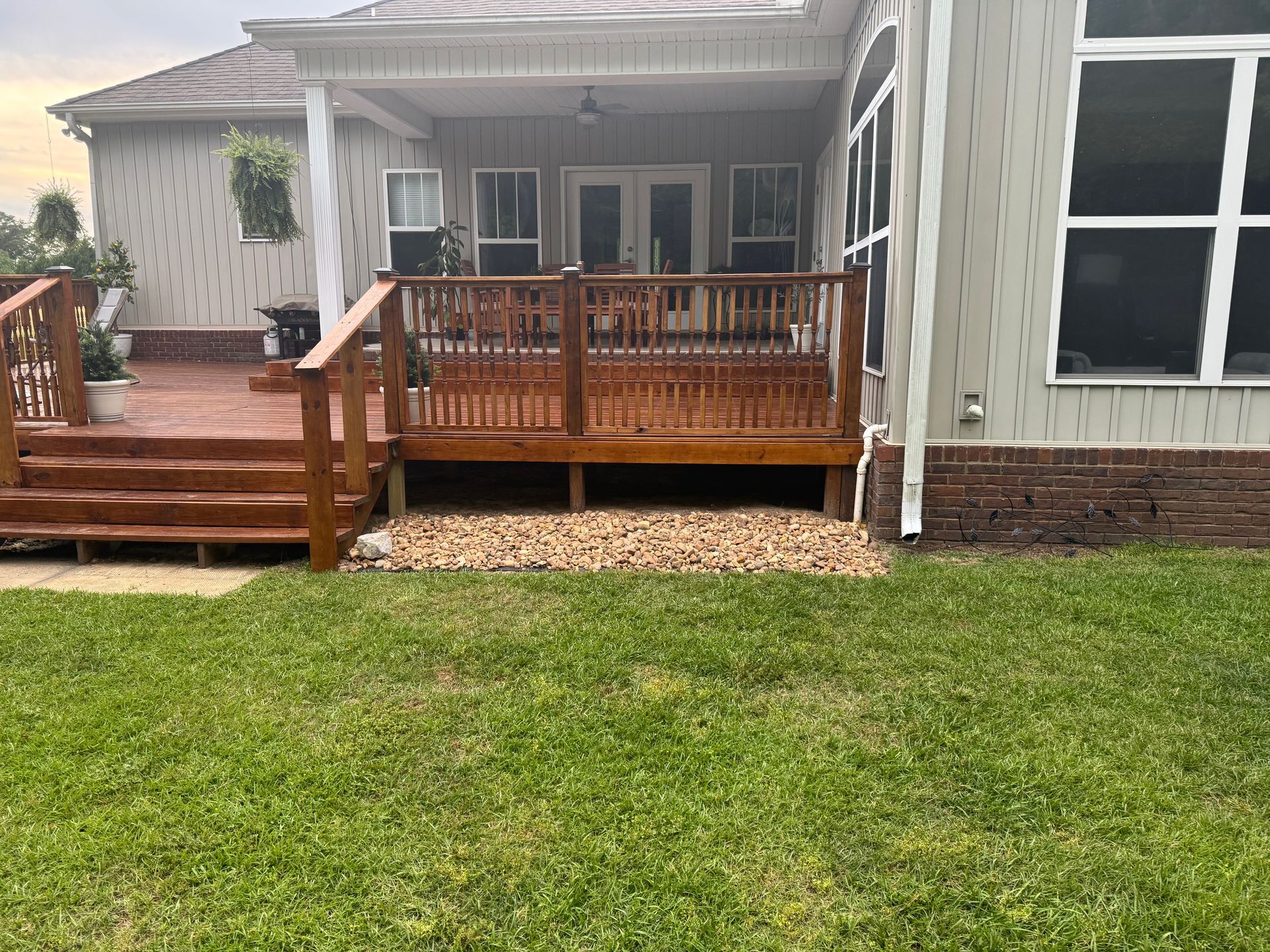 Wooden deck attached to a house with gravel underneath, surrounded by grass.