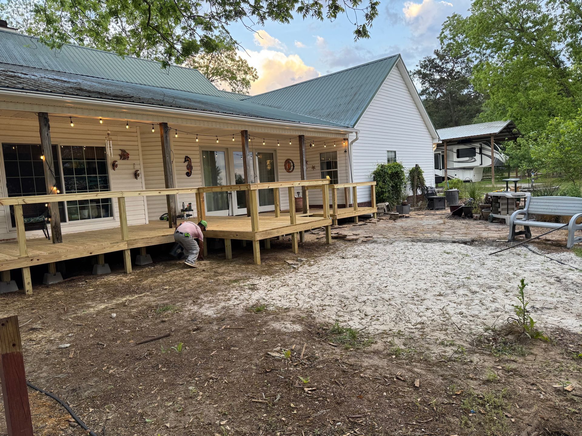 A white, rustic building with a wraparound porch, string lights, and a gravel yard.