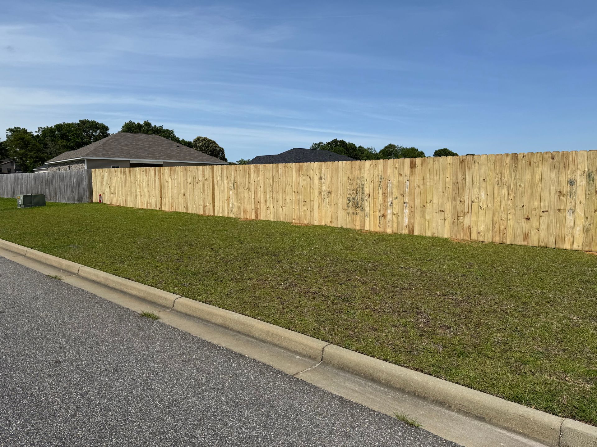 Wooden fence along a grassy slope, adjacent to a road, under a blue sky.