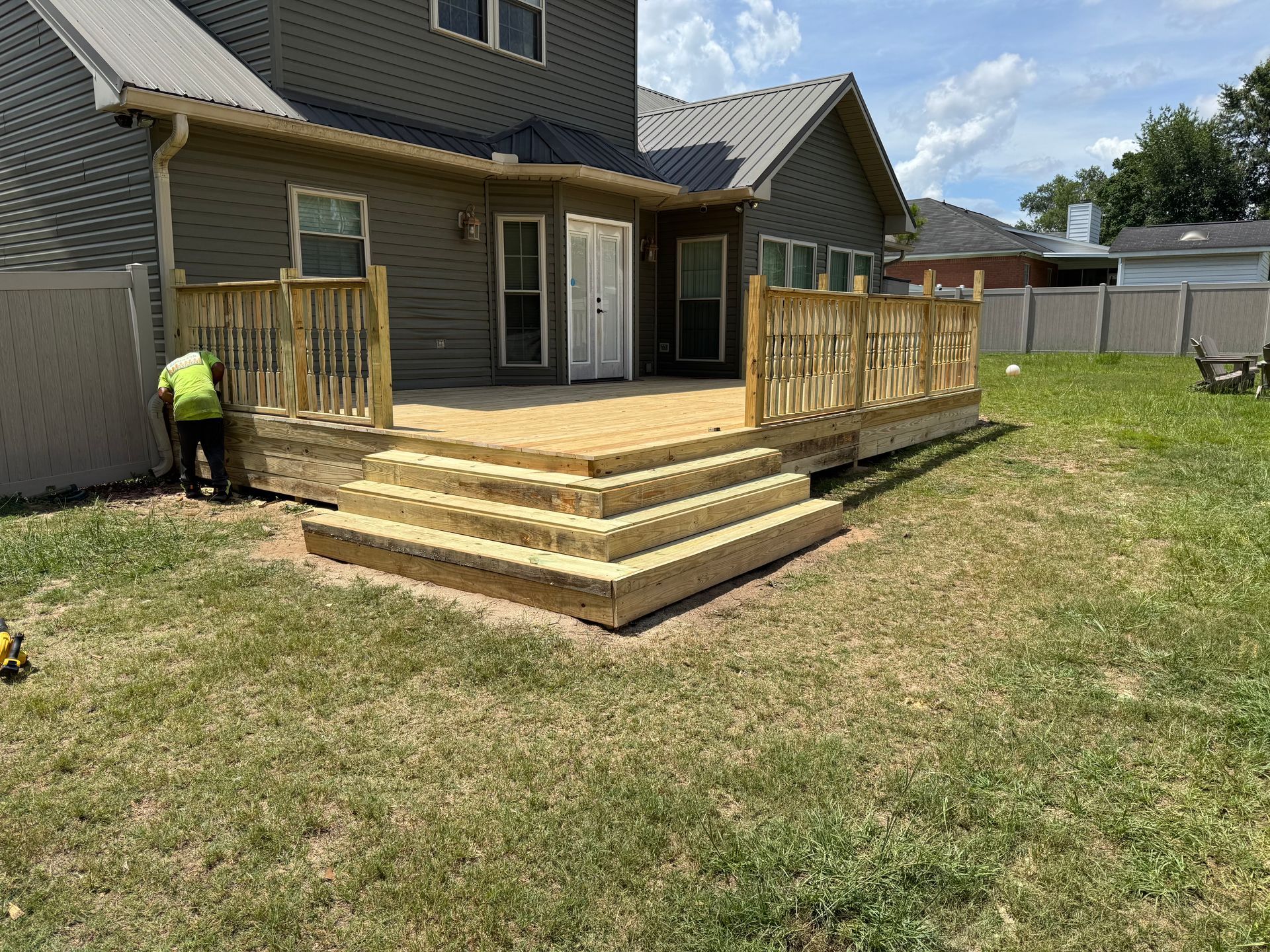 Backyard deck with wooden steps and railing, person in yellow vest is working on it.
