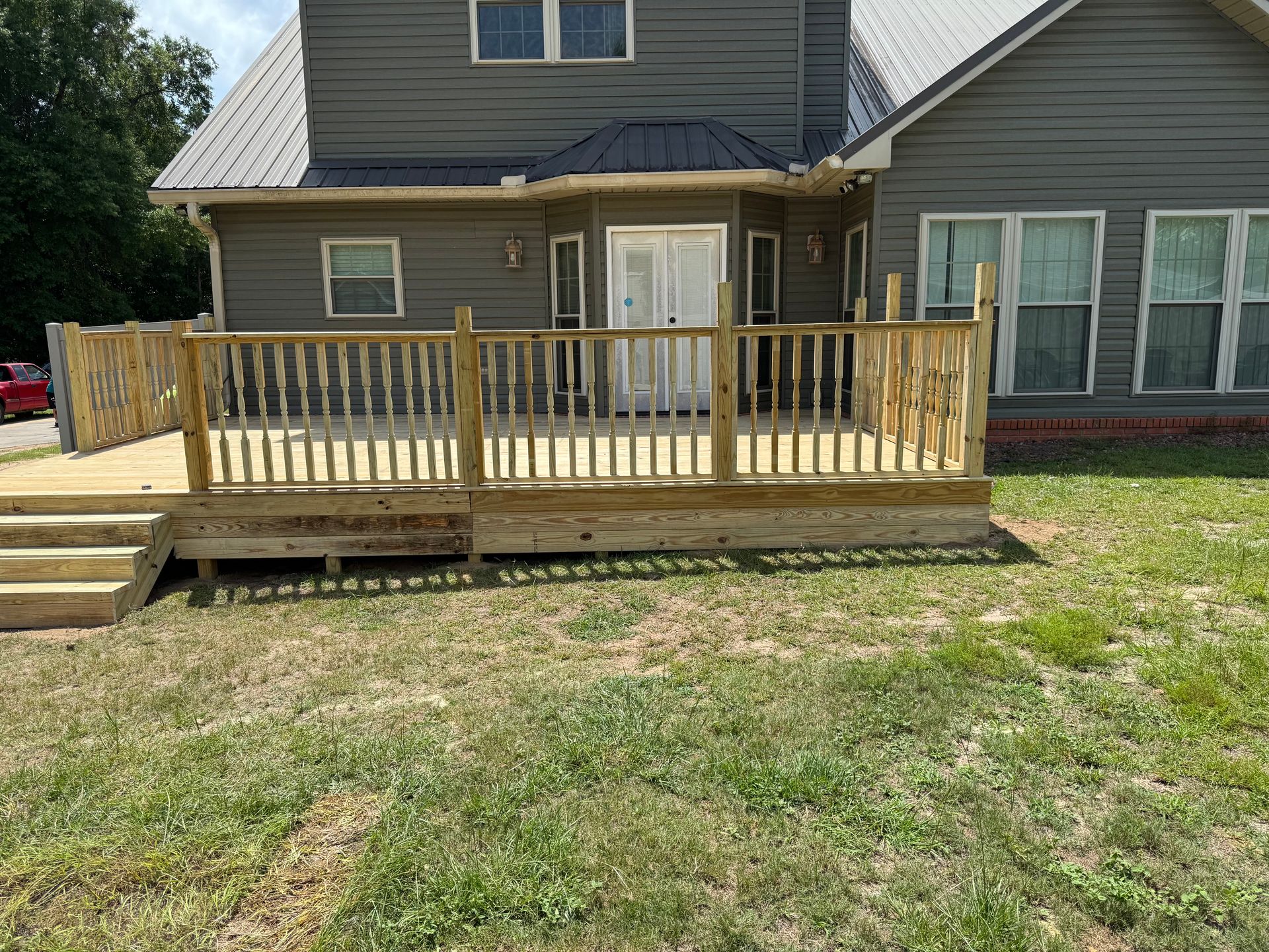 Wooden deck attached to a gray house, with a grass yard in the foreground.