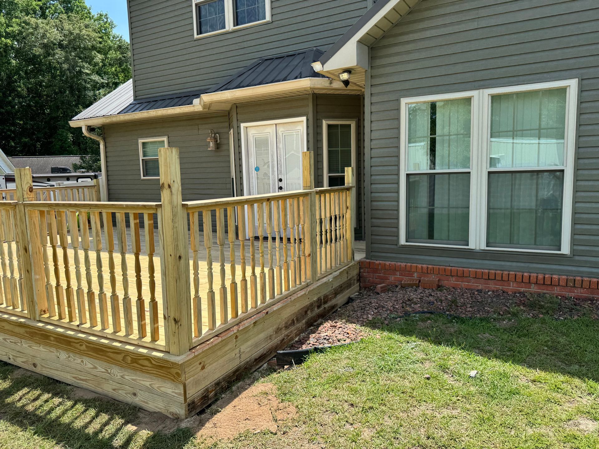 Wooden deck attached to a gray house, next to a grassy yard.