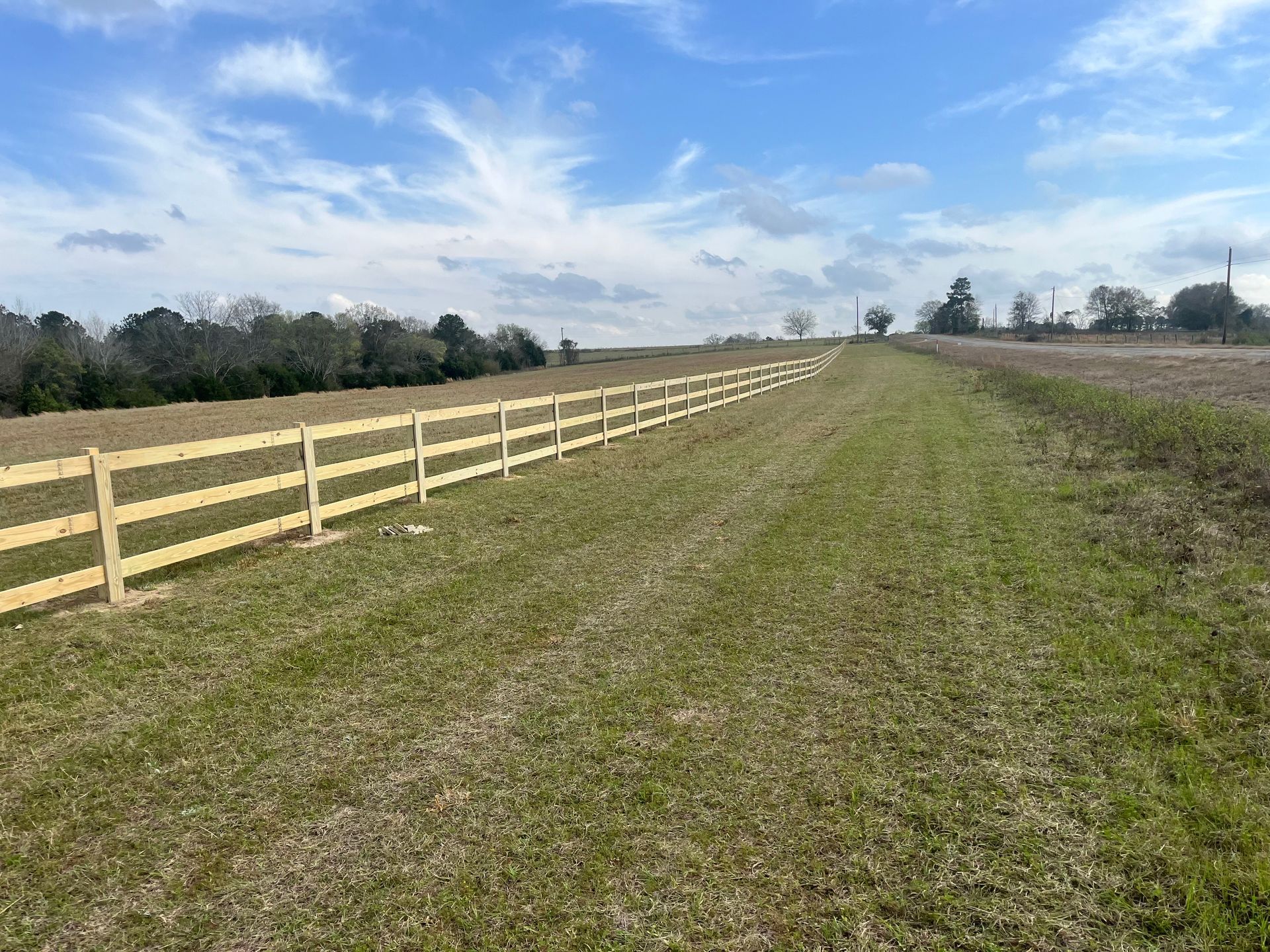 A wooden fence spans a grassy field under a partly cloudy sky.