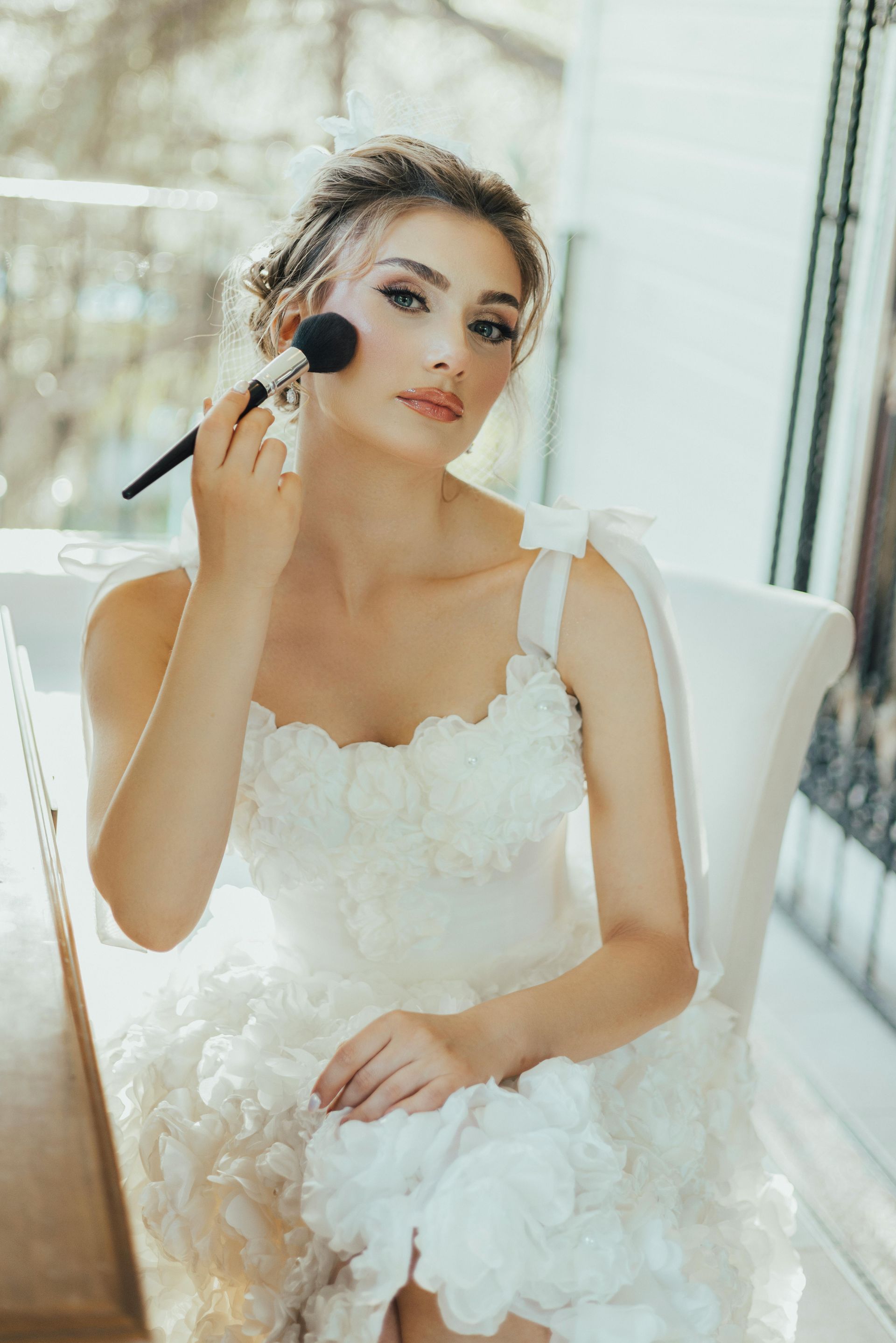 A woman in a wedding dress is applying makeup to her face with a brush.